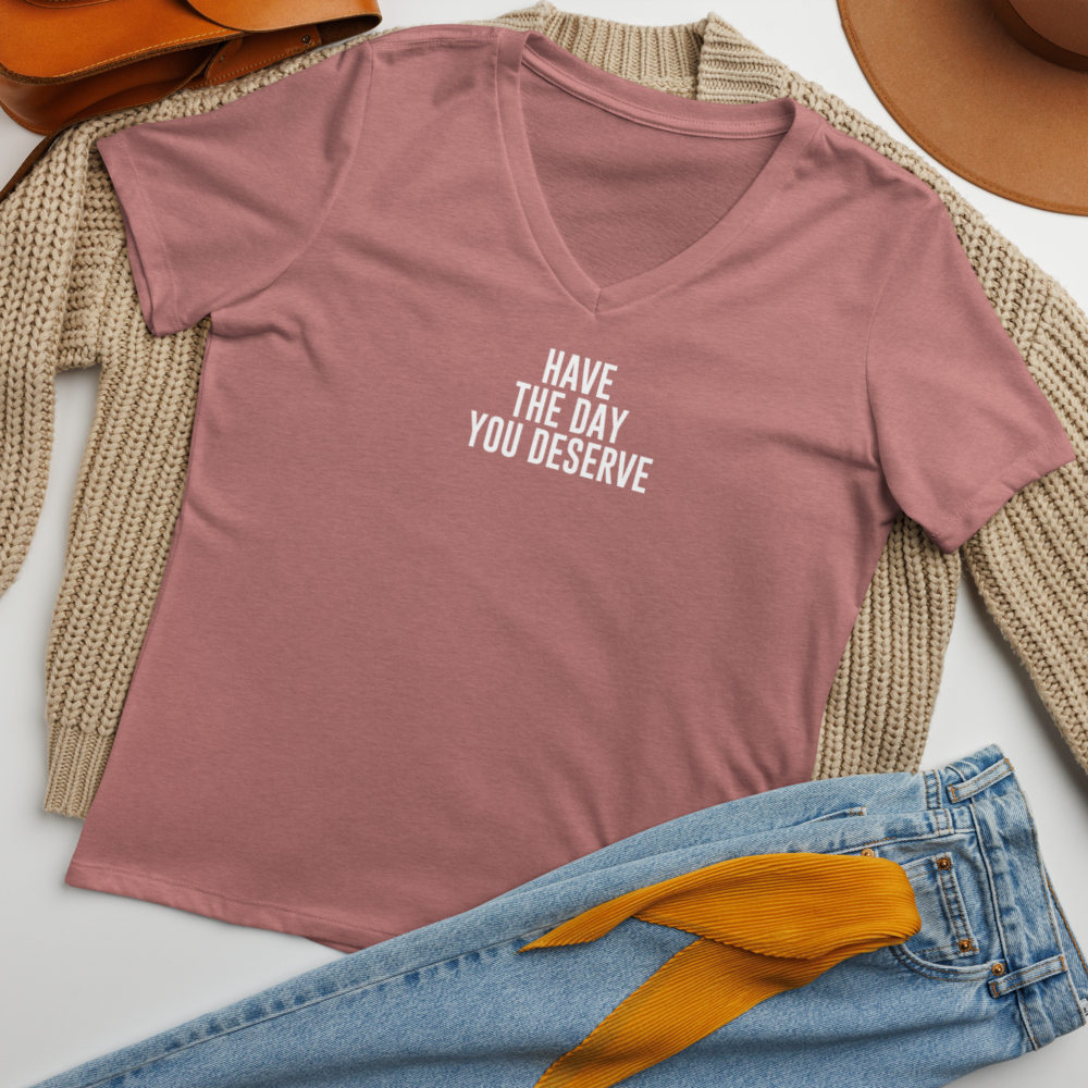 "Have the day you deserve" printed on a heather mauve women's relaxed v-neck t-shirt laying on a flat surface amongst other clothes