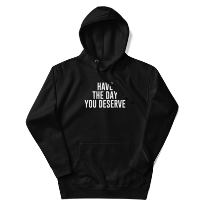 "Have the day you deserve" printed on a black unisex hoodie laying on a flat surface with the hood up