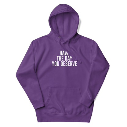 "Have the day you deserve" printed on a purple unisex hoodie laying on a flat surface with the hood up
