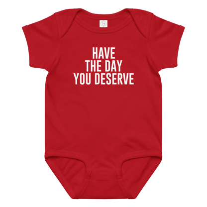 "Have the day you deserve" printed on a red baby jersey bodysuit laying on a flat surface amongst other clothes