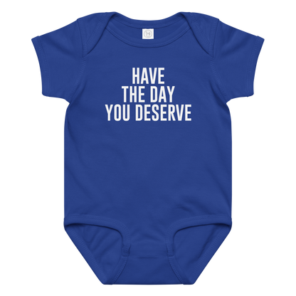 "Have the day you deserve" printed on a royal baby jersey bodysuit laying on a flat surface amongst other clothes