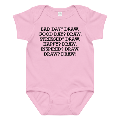 "Bad Day? Draw. Good Day? Draw. Stressed? Draw. Happy? Draw. Inspired? Draw. Draw? Draw!" printed on a pink baby jersey bodysuit laying on a flat surface amongst other clothes