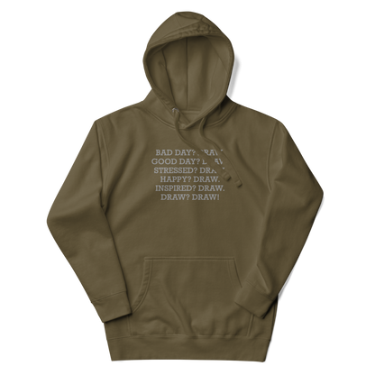 "Bad Day? Draw. Good Day? Draw. Stressed? Draw. Happy? Draw. Inspired? Draw. Draw? Draw!" printed on a military green unisex hoodie laying on a flat surface with the hood up