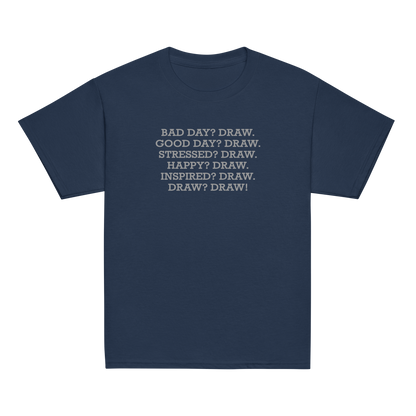"Bad Day? Draw. Good Day? Draw. Stressed? Draw. Happy? Draw. Inspired? Draw. Draw? Draw!" printed on a navy youth classic tee laying on a flat surface