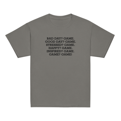 "Bad Day? Game. Good Day? Game. Stressed? Game. Happy? Game. Inspired? Game. Game? Game!" printed on a charcoal youth classic tee laying on a flat surface