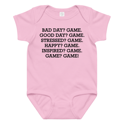 "Bad Day? Game. Good Day? Game. Stressed? Game. Happy? Game. Inspired? Game. Game? Game!" printed on a pink baby jersey bodysuit laying on a flat surface amongst other clothes