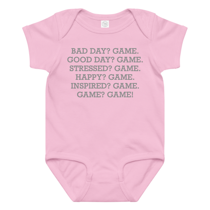 "Bad Day? Game. Good Day? Game. Stressed? Game. Happy? Game. Inspired? Game. Game? Game!" printed on a pink baby jersey bodysuit laying on a flat surface amongst other clothes