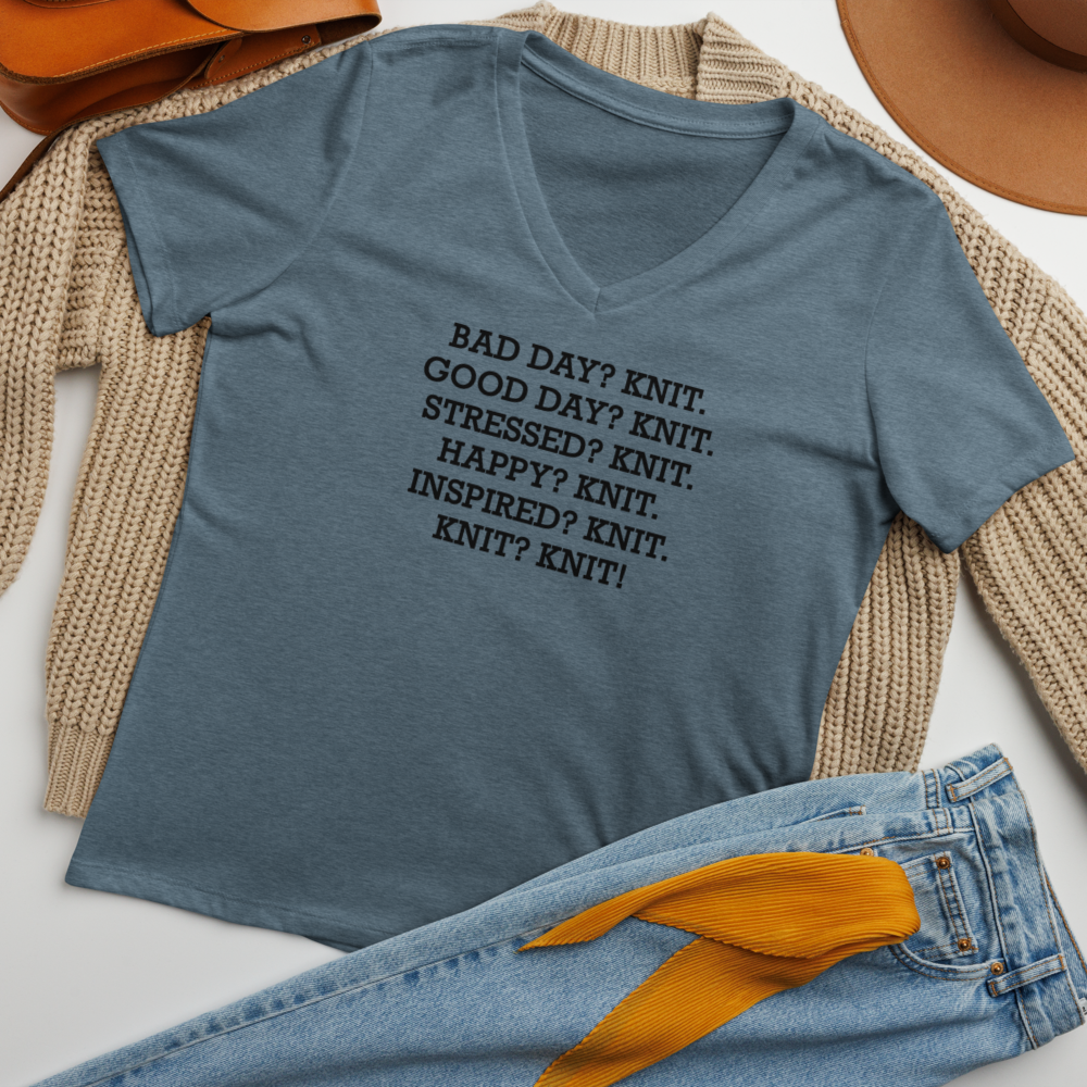 "Bad Day? Knit. Good Day? Knit. Stressed? Knit. Happy? Knit. Inspired? Knit. Knit? Knit!" printed on a heather slate women's relaxed v-neck t-shirt laying on a flat surface amongst other clothes