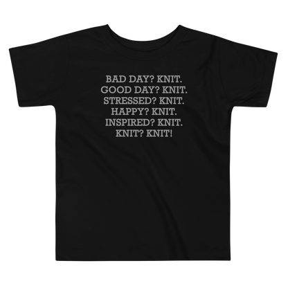 "Bad Day? Knit. Good Day? Knit. Stressed? Knit. Happy? Knit. Inspired? Knit. Knit? Knit!" printed on a black toddler short sleeve tee laying on a flat surface