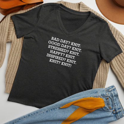 "Bad Day? Knit. Good Day? Knit. Stressed? Knit. Happy? Knit. Inspired? Knit. Knit? Knit!" printed on a dark grey heather women's relaxed v-neck t-shirt laying on a flat surface amongst other clothes