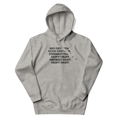 "Bad Day? Paint. Good Day? Paint. Stressed? Paint. Happy? Paint. Inspired? Paint. Paint? Paint!" printed on a carbon grey unisex hoodie laying on a flat surface with the hood up