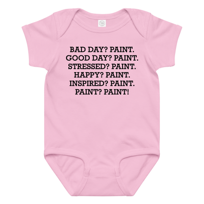 "Bad Day? Paint. Good Day? Paint. Stressed? Paint. Happy? Paint. Inspired? Paint. Paint? Paint!" printed on a pink baby jersey bodysuit laying on a flat surface amongst other clothes