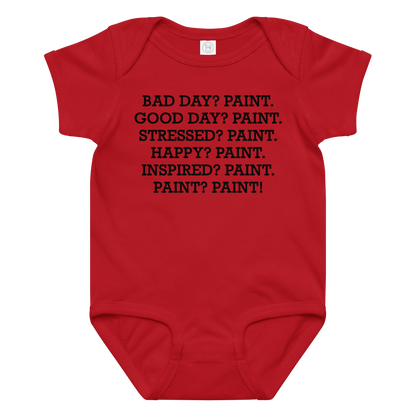 "Bad Day? Paint. Good Day? Paint. Stressed? Paint. Happy? Paint. Inspired? Paint. Paint? Paint!" printed on a red baby jersey bodysuit laying on a flat surface amongst other clothes
