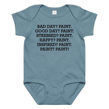 "Bad Day? Paint. Good Day? Paint. Stressed? Paint. Happy? Paint. Inspired? Paint. Paint? Paint!" printed on a vintage indigo baby jersey bodysuit laying on a flat surface amongst other clothes