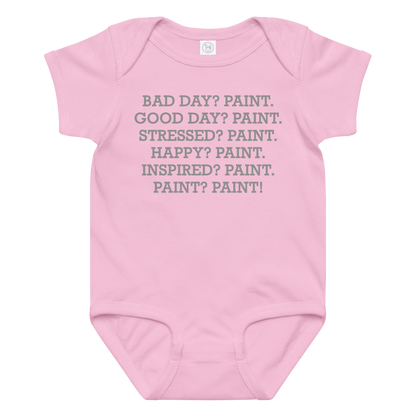 "Bad Day? Paint. Good Day? Paint. Stressed? Paint. Happy? Paint. Inspired? Paint. Paint? Paint!" printed on a pink baby jersey bodysuit laying on a flat surface amongst other clothes