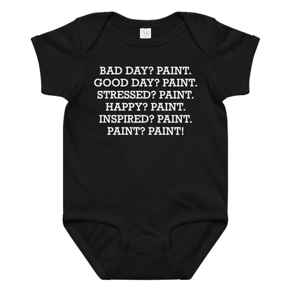 "Bad Day? Paint. Good Day? Paint. Stressed? Paint. Happy? Paint. Inspired? Paint. Paint? Paint!" printed on a black baby jersey bodysuit laying on a flat surface amongst other clothes