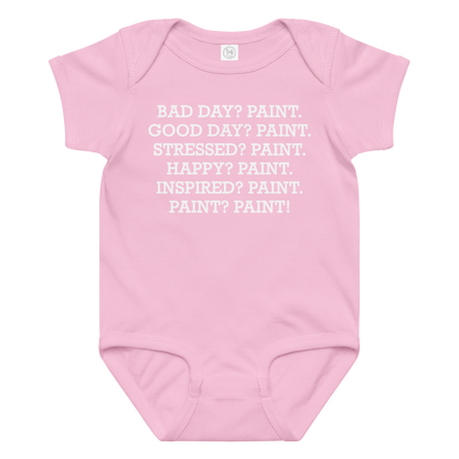 "Bad Day? Paint. Good Day? Paint. Stressed? Paint. Happy? Paint. Inspired? Paint. Paint? Paint!" printed on a pink baby jersey bodysuit laying on a flat surface amongst other clothes