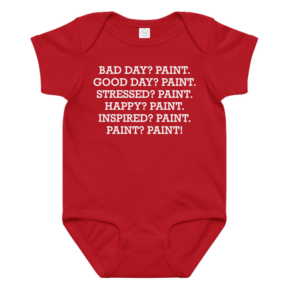 "Bad Day? Paint. Good Day? Paint. Stressed? Paint. Happy? Paint. Inspired? Paint. Paint? Paint!" printed on a red baby jersey bodysuit laying on a flat surface amongst other clothes