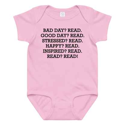 "Bad Day? Read. Good Day? Read. Stressed? Read. Happy? Read. Inspired? Read. Read? Read!" printed on a pink baby jersey bodysuit laying on a flat surface amongst other clothes