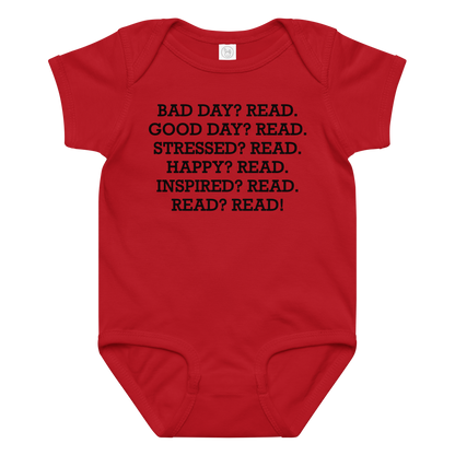 "Bad Day? Read. Good Day? Read. Stressed? Read. Happy? Read. Inspired? Read. Read? Read!" printed on a red baby jersey bodysuit laying on a flat surface amongst other clothes