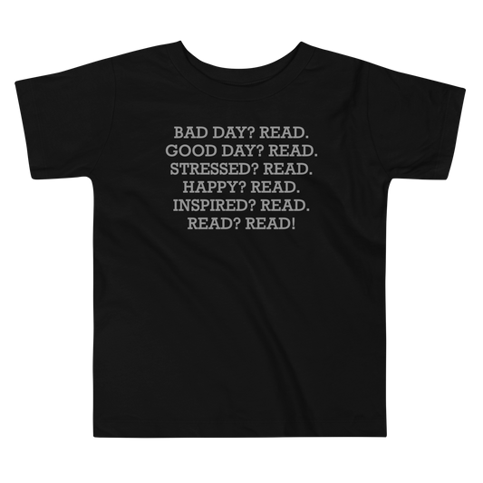 "Bad Day? Read. Good Day? Read. Stressed? Read. Happy? Read. Inspired? Read. Read? Read!" printed on a black toddler short sleeve tee laying on a flat surface