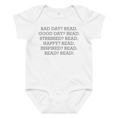 "Bad Day? Read. Good Day? Read. Stressed? Read. Happy? Read. Inspired? Read. Read? Read!" printed on a white baby jersey bodysuit laying on a flat surface amongst other clothes