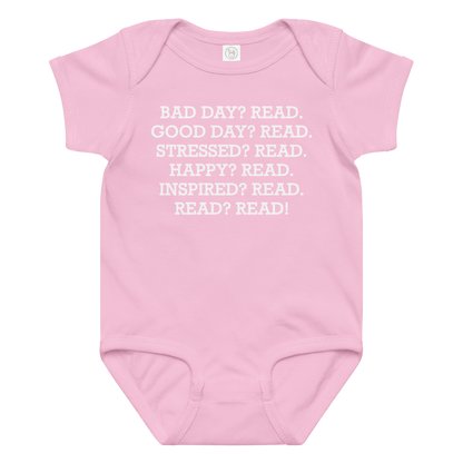"Bad Day? Read. Good Day? Read. Stressed? Read. Happy? Read. Inspired? Read. Read? Read!" printed on a pink baby jersey bodysuit laying on a flat surface amongst other clothes