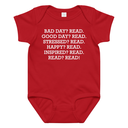 "Bad Day? Read. Good Day? Read. Stressed? Read. Happy? Read. Inspired? Read. Read? Read!" printed on a red baby jersey bodysuit laying on a flat surface amongst other clothes