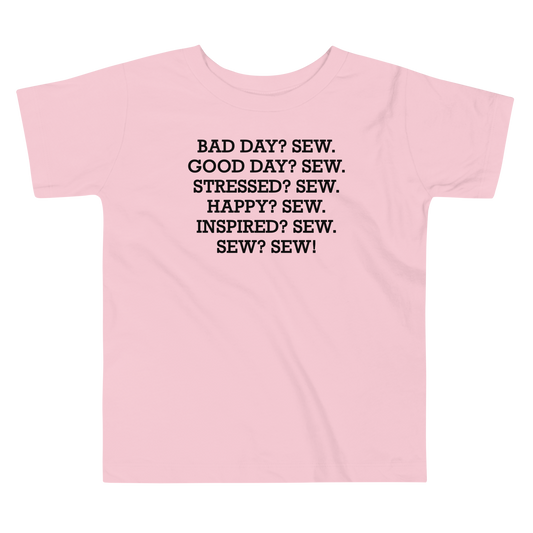 "Bad Day? Sew. Good Day? Sew. Stressed? Sew. Happy? Sew. Inspired? Sew. Sew? Sew!" printed on a pink toddler short sleeve tee laying on a flat surface