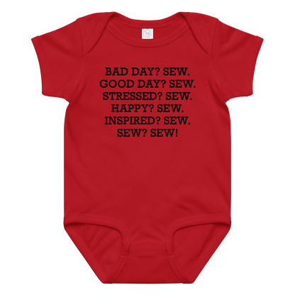 "Bad Day? Sew. Good Day? Sew. Stressed? Sew. Happy? Sew. Inspired? Sew. Sew? Sew!" printed on a red baby jersey bodysuit laying on a flat surface amongst other clothes