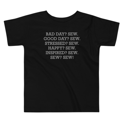"Bad Day? Sew. Good Day? Sew. Stressed? Sew. Happy? Sew. Inspired? Sew. Sew? Sew!" printed on a black toddler short sleeve tee laying on a flat surface