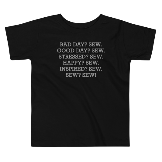 "Bad Day? Sew. Good Day? Sew. Stressed? Sew. Happy? Sew. Inspired? Sew. Sew? Sew!" printed on a black toddler short sleeve tee laying on a flat surface