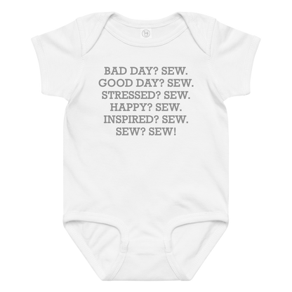 "Bad Day? Sew. Good Day? Sew. Stressed? Sew. Happy? Sew. Inspired? Sew. Sew? Sew!" printed on a white baby jersey bodysuit laying on a flat surface amongst other clothes