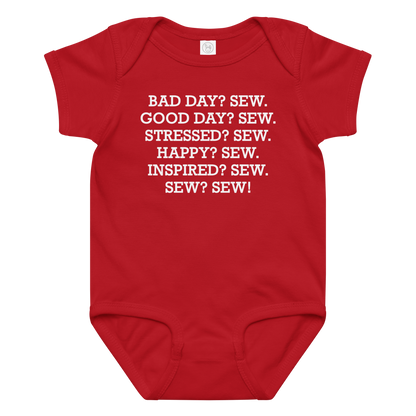 "Bad Day? Sew. Good Day? Sew. Stressed? Sew. Happy? Sew. Inspired? Sew. Sew? Sew!" printed on a red baby jersey bodysuit laying on a flat surface amongst other clothes