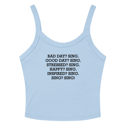 "Bad Day? Sing. Good Day? Sing. Stressed? Sing. Happy? Sing. Inspired? Sing. Sing? Sing!" printed on a solid baby blue blend women's micro-rib tanktop laying on a flat surface amongst sunglasses and shorts