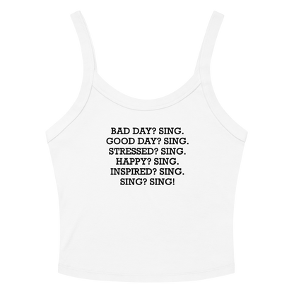 "Bad Day? Sing. Good Day? Sing. Stressed? Sing. Happy? Sing. Inspired? Sing. Sing? Sing!" printed on a solid white blend women's micro-rib tanktop laying on a flat surface amongst sunglasses and shorts