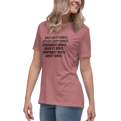 "Bad Day? Sing. Good Day? Sing. Stressed? Sing. Happy? Sing. Inspired? Sing. Sing? Sing!" printed on a heather mauve women's relaxed t-shirt worn by a female