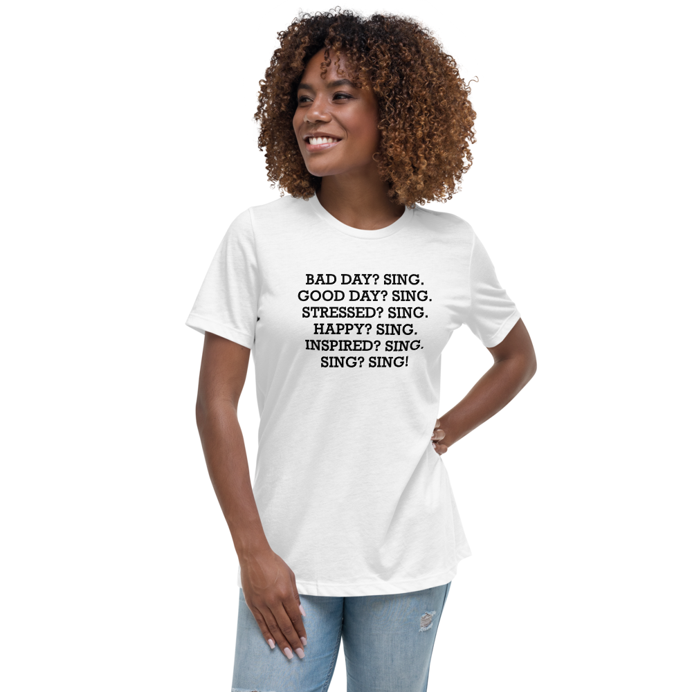 "Bad Day? Sing. Good Day? Sing. Stressed? Sing. Happy? Sing. Inspired? Sing. Sing? Sing!" printed on a white women's relaxed t-shirt worn by a female