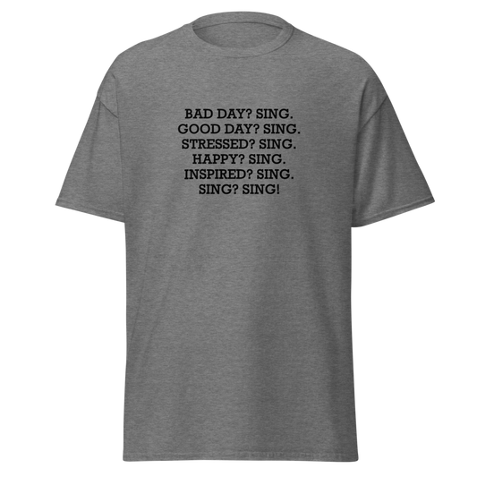 "Bad Day? Sing. Good Day? Sing. Stressed? Sing. Happy? Sing. Inspired? Sing. Sing? Sing!" printed on a graphite heather unisex classic tee laying on a flat surface