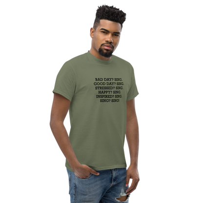 "Bad Day? Sing. Good Day? Sing. Stressed? Sing. Happy? Sing. Inspired? Sing. Sing? Sing!" printed on a military green unisex classic tee worn by a male