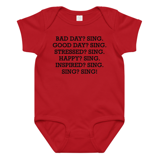 "Bad Day? Sing. Good Day? Sing. Stressed? Sing. Happy? Sing. Inspired? Sing. Sing? Sing!" printed on a red baby jersey bodysuit laying on a flat surface amongst other clothes
