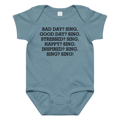 "Bad Day? Sing. Good Day? Sing. Stressed? Sing. Happy? Sing. Inspired? Sing. Sing? Sing!" printed on a vintage indigo baby jersey bodysuit laying on a flat surface amongst other clothes
