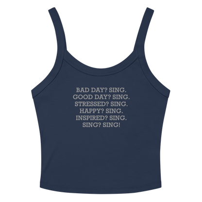 "Bad Day? Sing. Good Day? Sing. Stressed? Sing. Happy? Sing. Inspired? Sing. Sing? Sing!" printed on a solid navy blend women's micro-rib tanktop laying on a flat surface amongst sunglasses and shorts