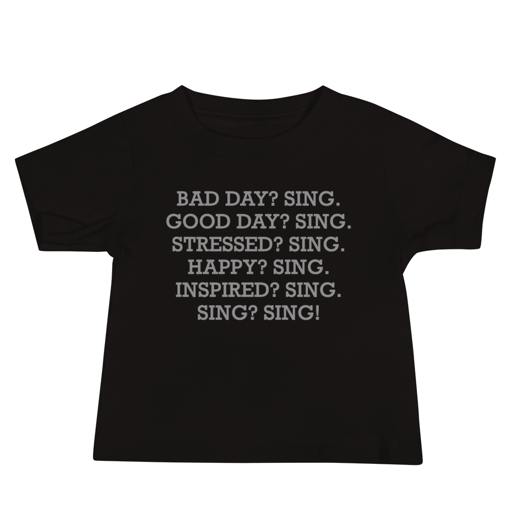 "Bad Day? Sing. Good Day? Sing. Stressed? Sing. Happy? Sing. Inspired? Sing. Sing? Sing!" printed on a black baby jersey short sleeve tee laying on a flat surface