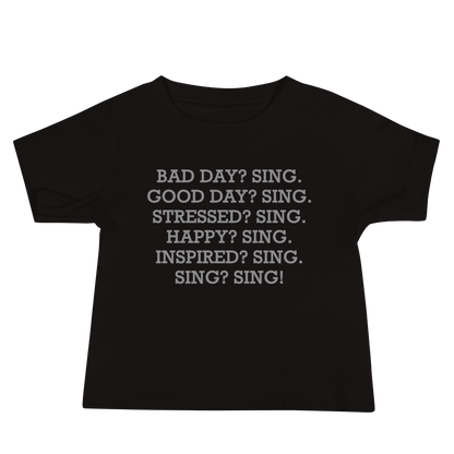 "Bad Day? Sing. Good Day? Sing. Stressed? Sing. Happy? Sing. Inspired? Sing. Sing? Sing!" printed on a black baby jersey short sleeve tee laying on a flat surface