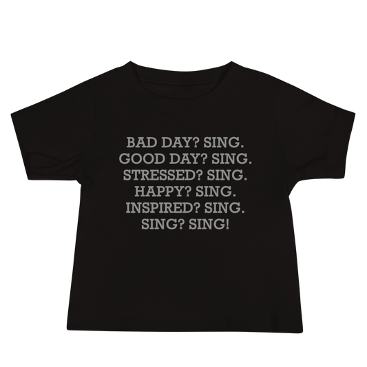 "Bad Day? Sing. Good Day? Sing. Stressed? Sing. Happy? Sing. Inspired? Sing. Sing? Sing!" printed on a black baby jersey short sleeve tee laying on a flat surface