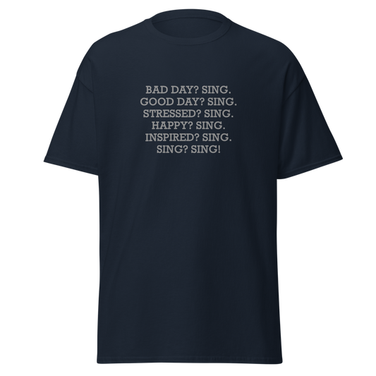 "Bad Day? Sing. Good Day? Sing. Stressed? Sing. Happy? Sing. Inspired? Sing. Sing? Sing!" printed on a navy unisex classic tee laying on a flat surface
