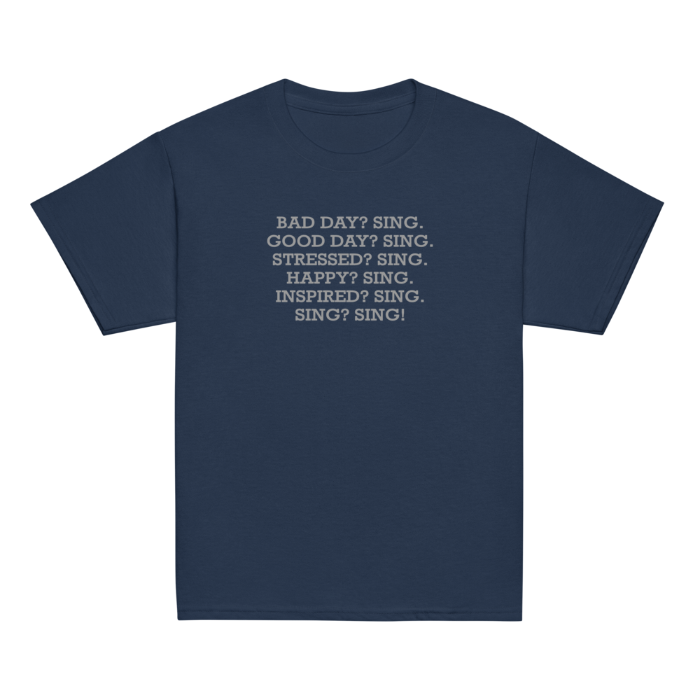 "Bad Day? Sing. Good Day? Sing. Stressed? Sing. Happy? Sing. Inspired? Sing. Sing? Sing!" printed on a navy youth classic tee laying on a flat surface