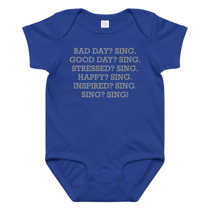 "Bad Day? Sing. Good Day? Sing. Stressed? Sing. Happy? Sing. Inspired? Sing. Sing? Sing!" printed on a royal baby jersey bodysuit laying on a flat surface amongst other clothes