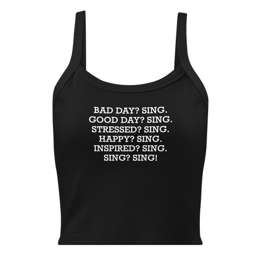 "Bad Day? Sing. Good Day? Sing. Stressed? Sing. Happy? Sing. Inspired? Sing. Sing? Sing!" printed on a solid black blend women's micro-rib tanktop laying on a flat surface